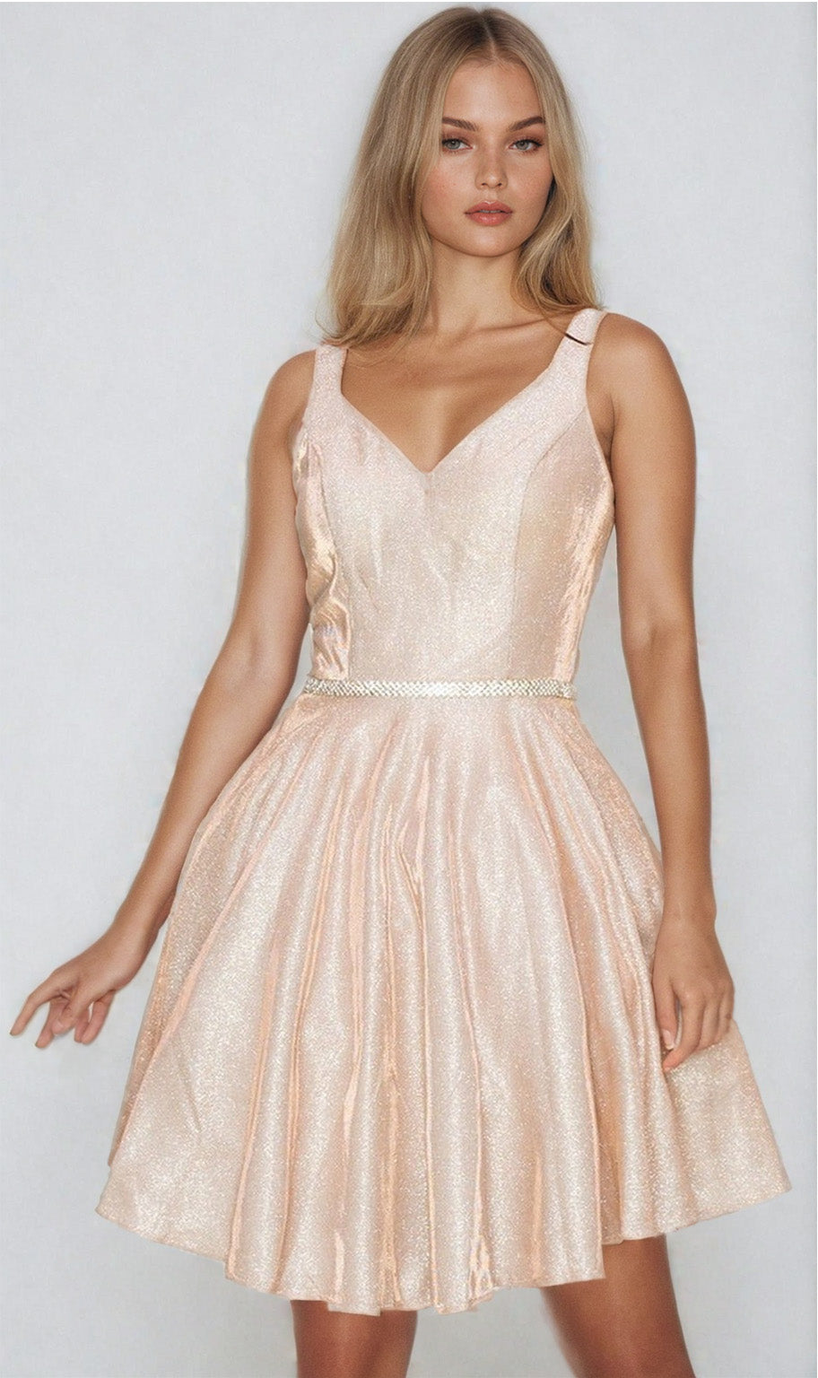 Woman wearing the Short A-Line Glitter Homecoming Dress 8013J—a sleeveless, light pink, shimmery dress with a V-neckline and decorative waistband—stands against a plain light background.